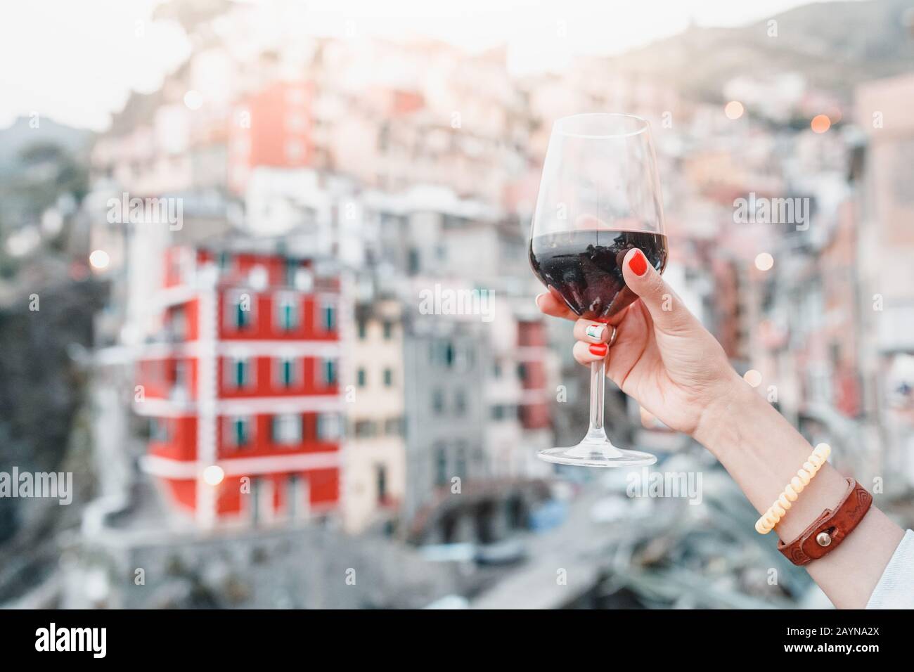 Female hand with italian flag nail art holding glass with red wine on a background of cinque terre riomaggiore town Stock Photo