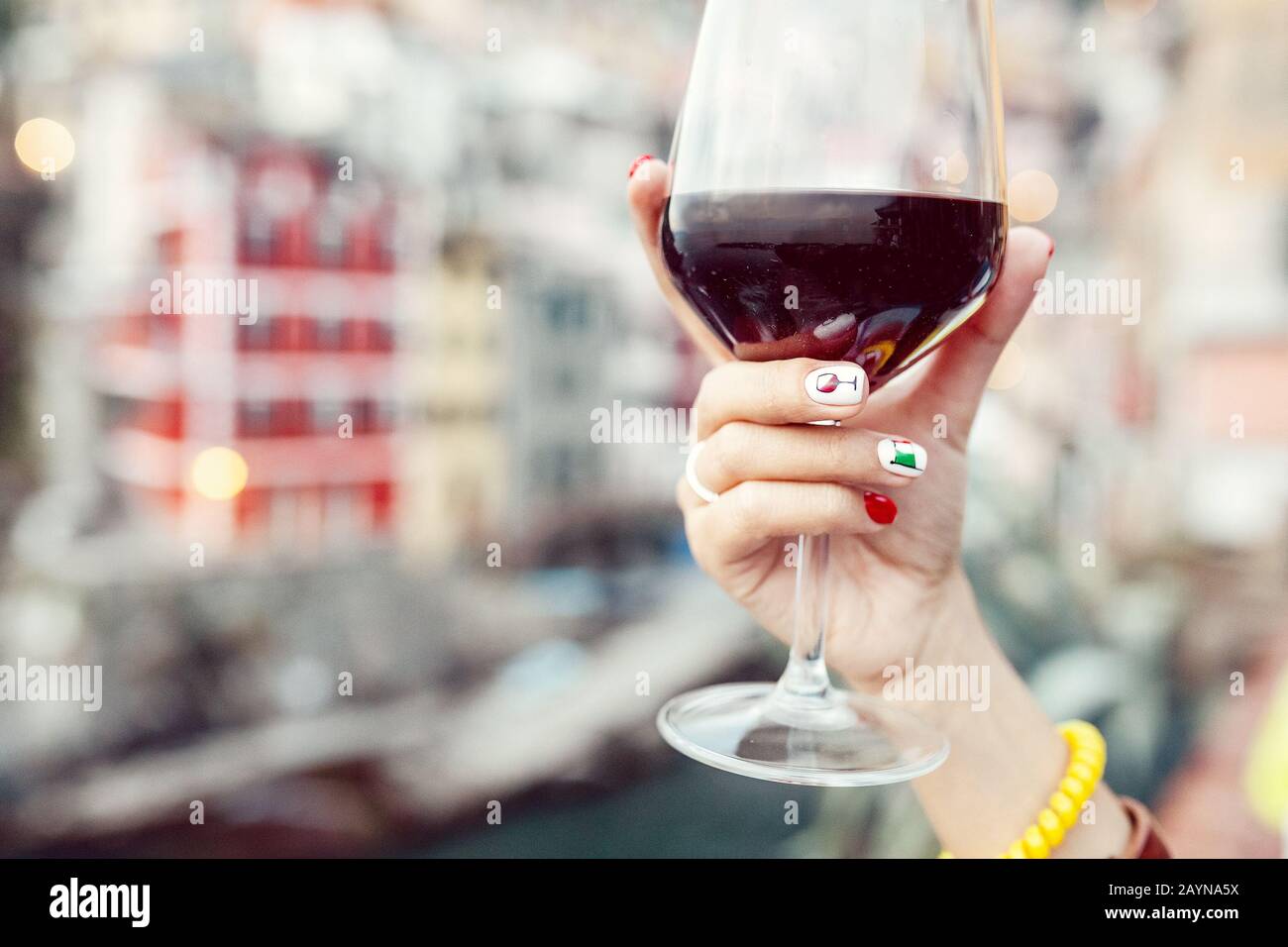 Female hand with italian flag nail art holding glass with red wine on a background of cinque terre riomaggiore town Stock Photo