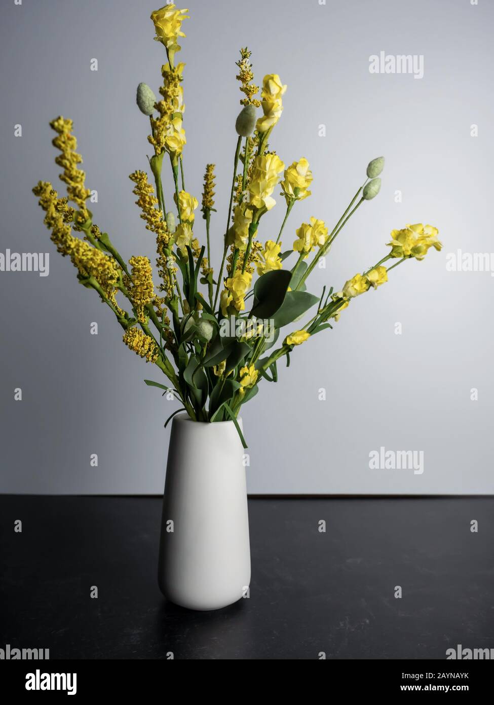 Yellow Artificial Flower Arrangement In A Simple White Base On A Black Slate And White Background Stock Photo Alamy