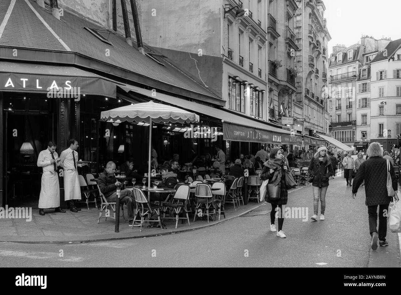 A black and white street scene in Paris with locals sitting outside at a restaurant and people walking through the street Stock Photo