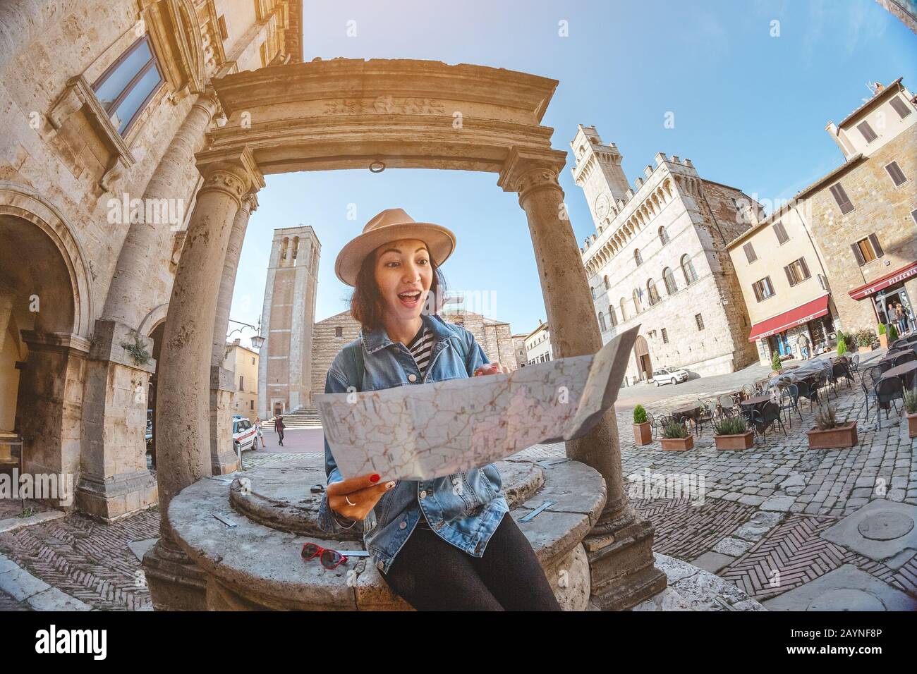 Happy asian tourist woman with map lost in old town of Montepulciano, Tuscany. Vacation and travel in Italy concept Stock Photo