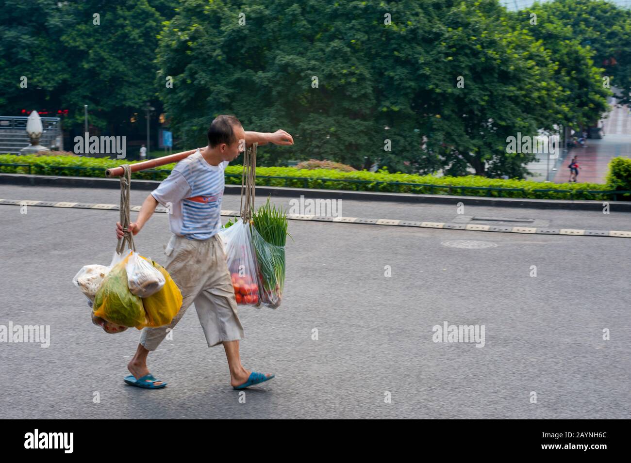 A man is carrying produce on a carrying pole, also called a shoulder