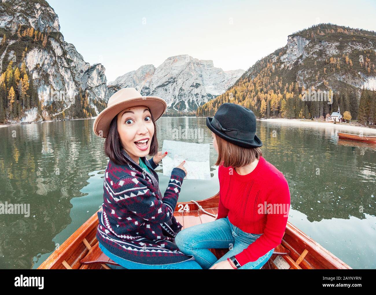 Two happy woman friends pointing to the map on the boat or canoe cruise tour on lago Di Braies lake in Italian Dolomites Alps Stock Photo