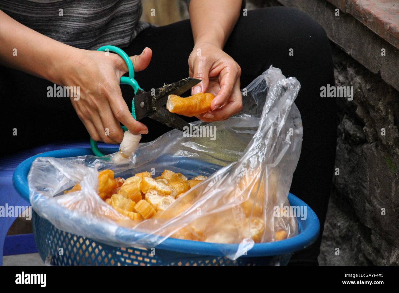 Vietnamese Fried Breadsticks (Dau Chao Quay) being cut to be use as soup side dish in the streets of Hanoi, Vietnam Stock Photo