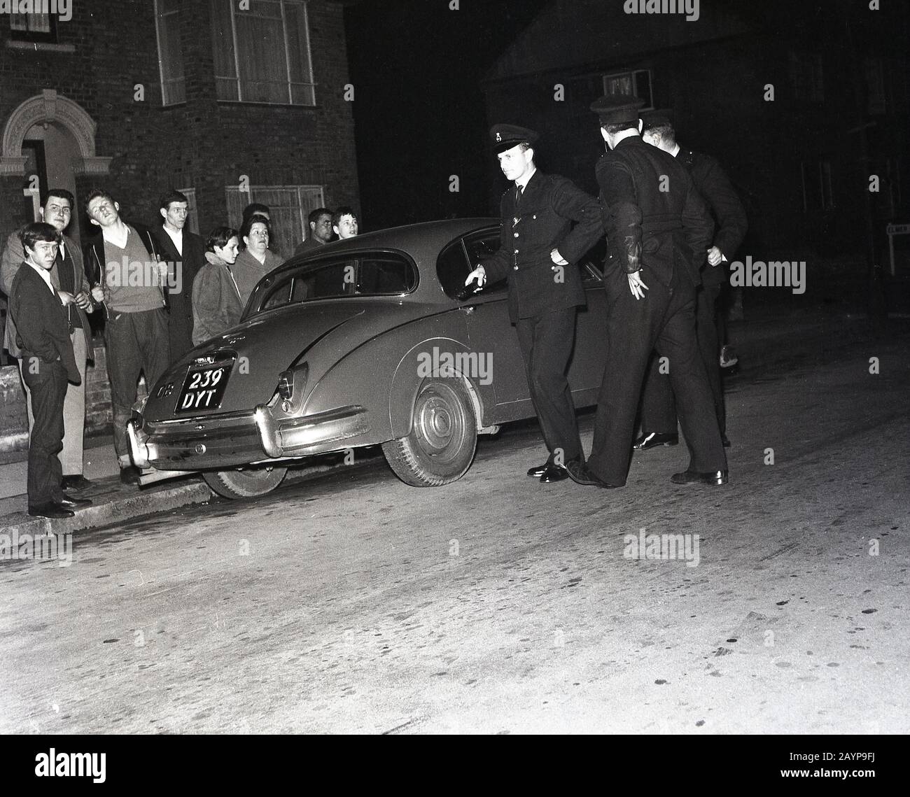 1960s, historical, eveningtime and uniformed policemen inspecting a Jaguar motor car parked in a street in New Cross, South London, England, UK. Stock Photo