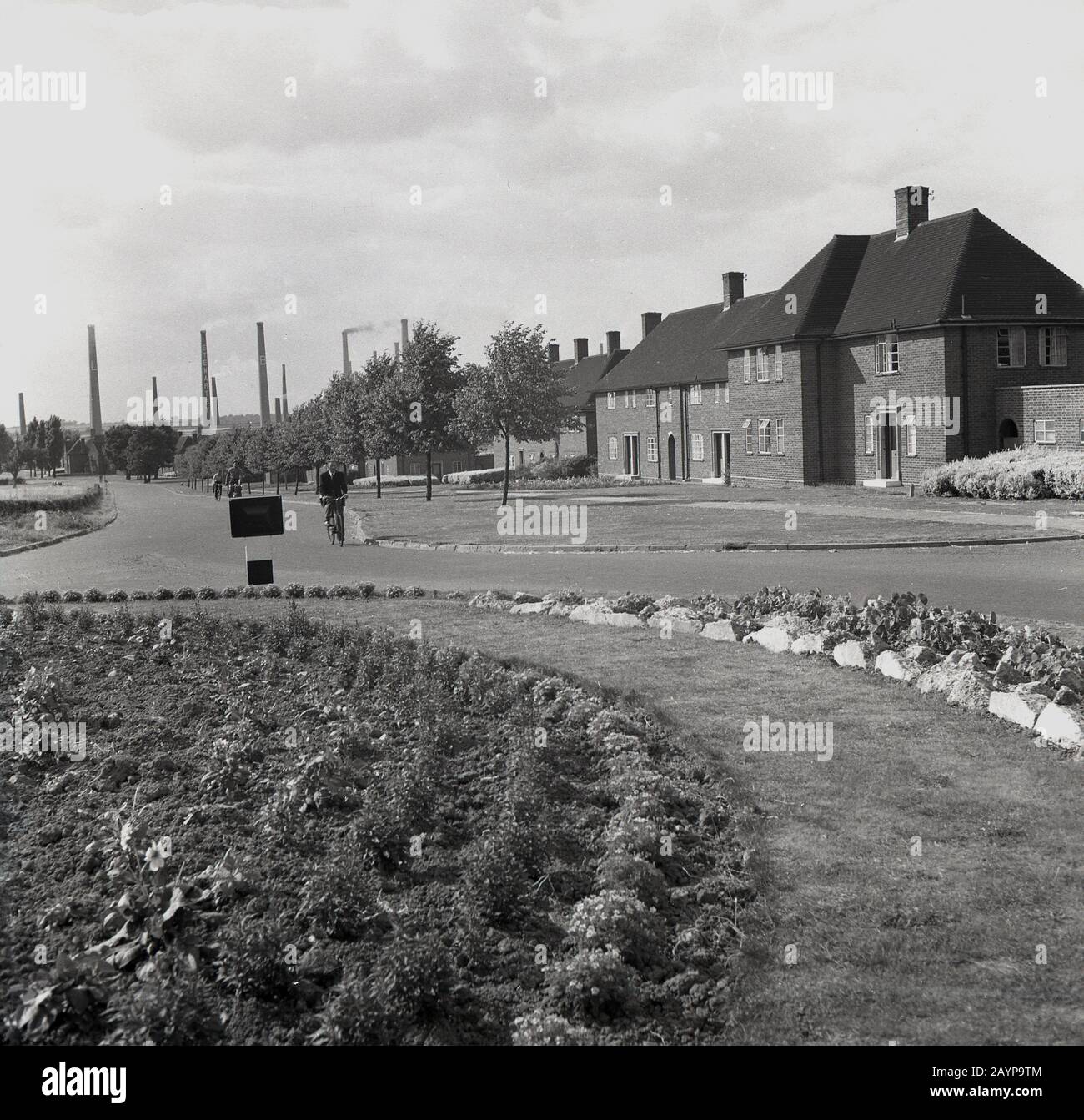 1950s, historical, an industrial worker cycling along a road at the housing estate outside of the London Brick Company, at the Stewartby brickworks, Bedford, England, UK. The company was a paternal employer in the mould of the victorian and quakers of the previous century and provided their workers with solid brick-built housing and extensive leisure facilities in a so-called 'model village'. Stock Photo
