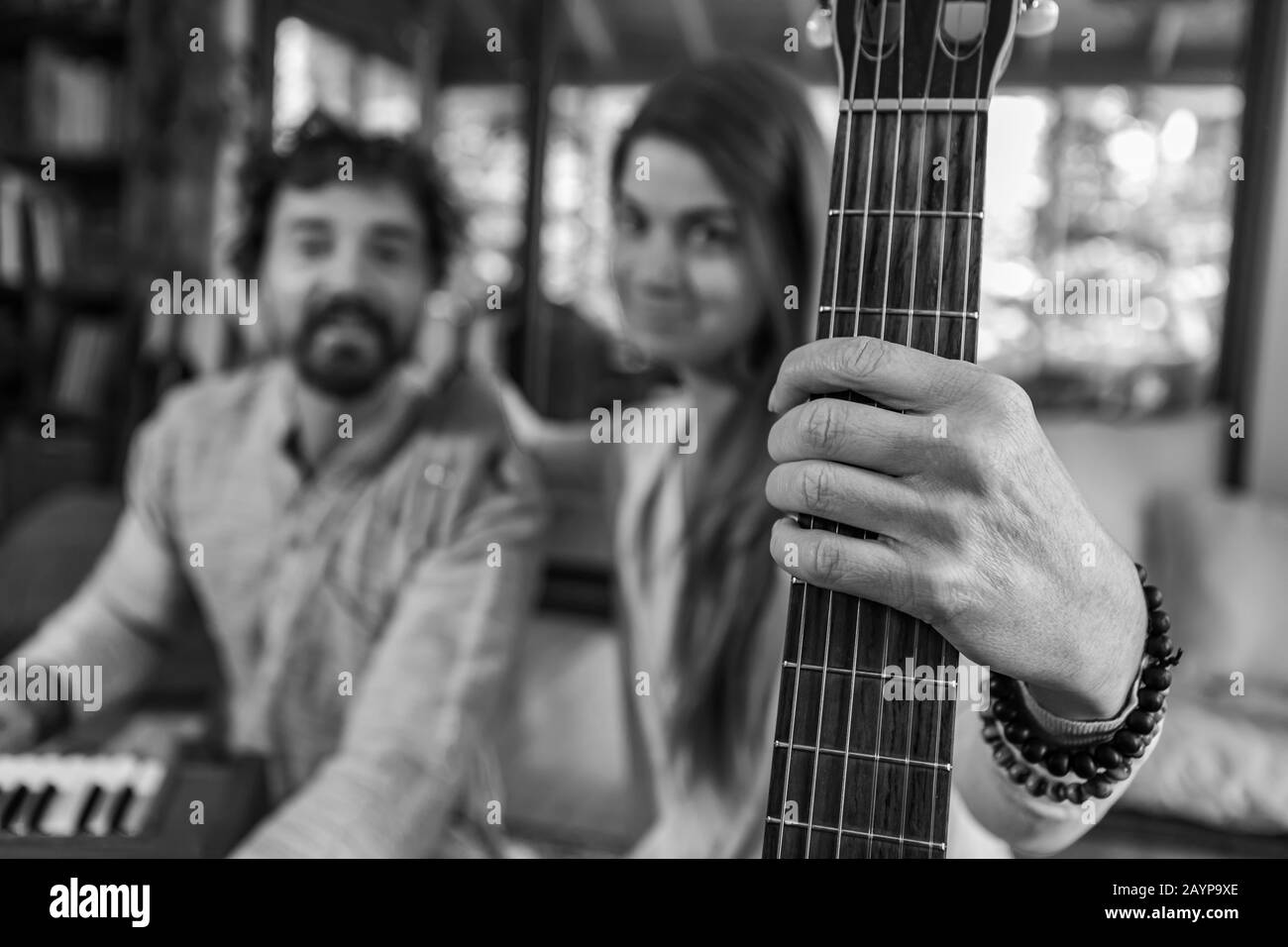 Black and white man and woman holding classical guitar with nylon strings and man playing harmonium for sacred and kirtan music looking at camera Stock Photo