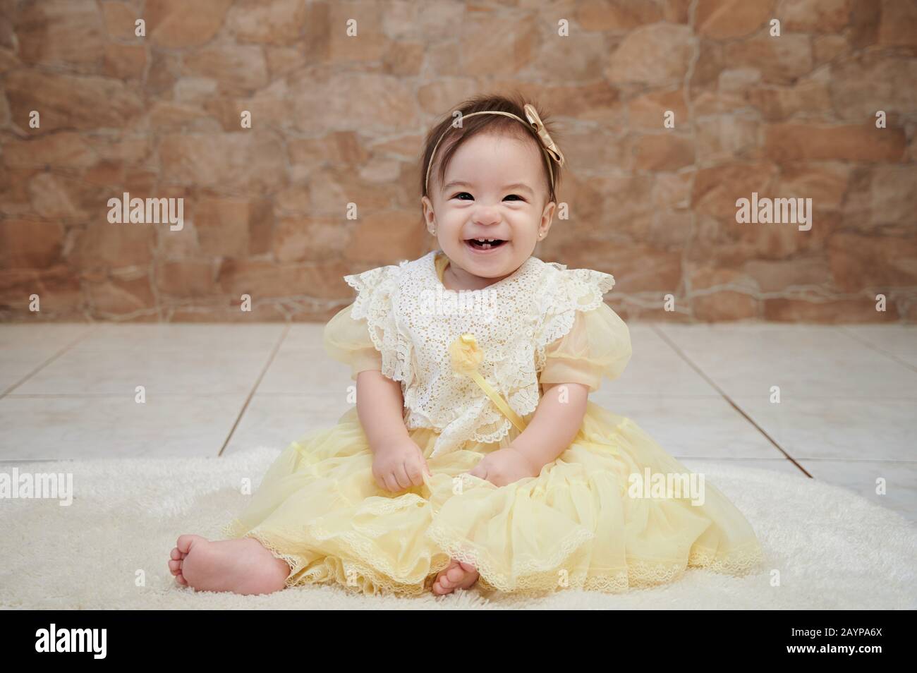 Happy smiling cute baby girl sit on floor in yellow dress Stock Photo