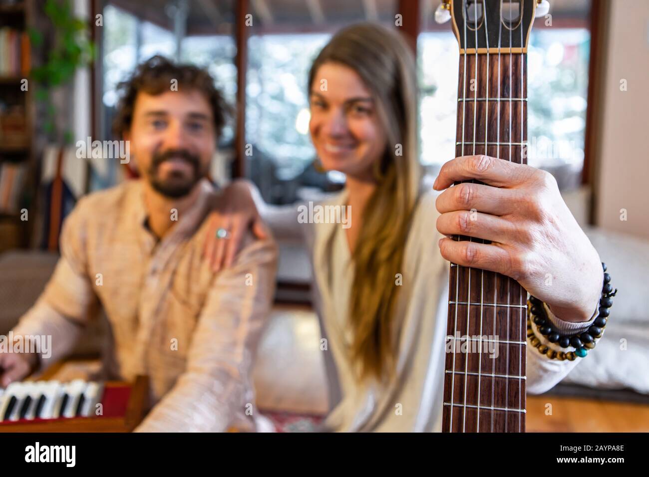 Shamanic man and woman holding classical guitar with nylon strings and man playing harmonium for sacred and kirtan music looking at camera Stock Photo