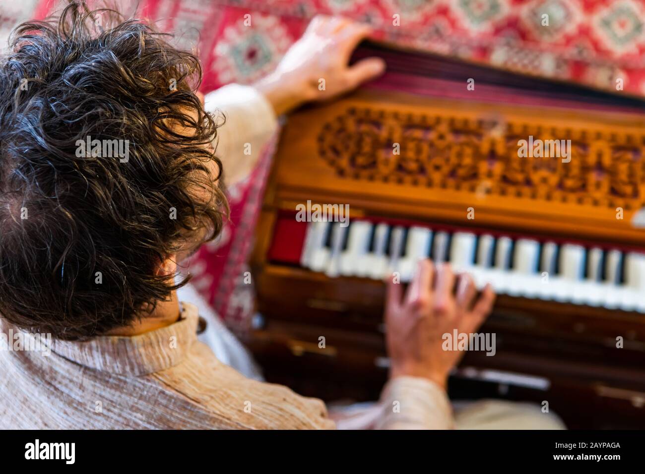 High angle view of young male shamanic playing kirtan music using musical instrument harmonium for meditation and positive vibrations Stock Photo