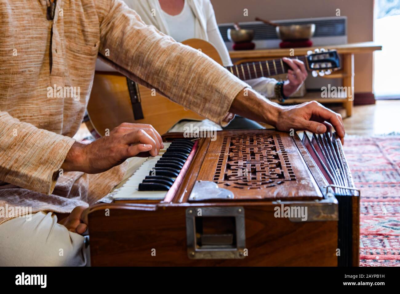 Closeup of male shaman hands playing sacred kirtan music with fingers on keys of harmonium with woman playing classical guitar in room to meditate Stock Photo