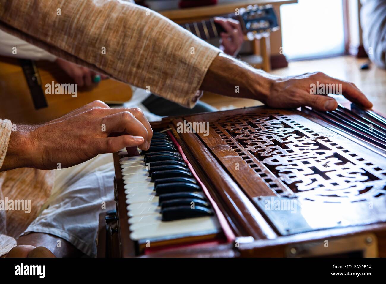 Closeup of male shamanic hands playing sacred kirtan music with fingers on keys of harmonium while sitting in room for peaceful meditation Stock Photo