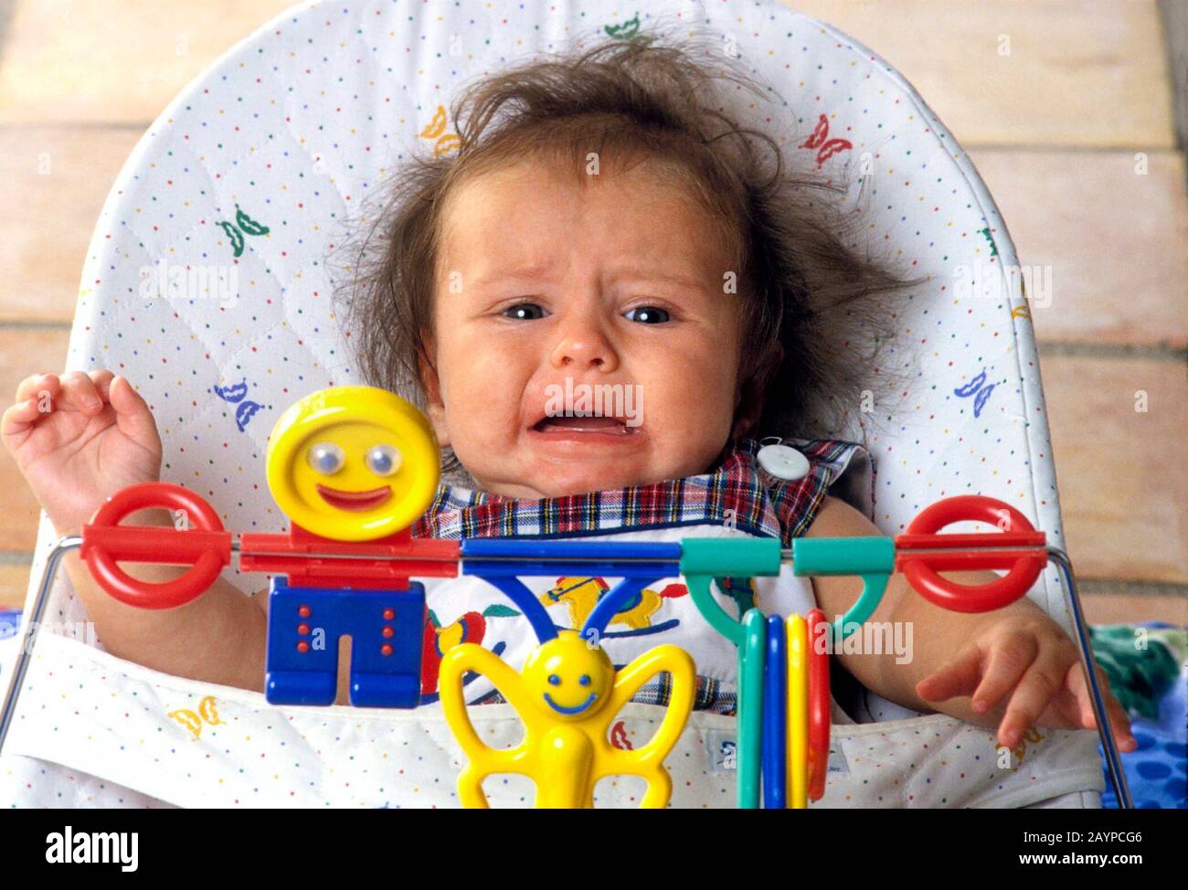 Austin, Texas USA: Fussy four-month-old baby boy in bouncer seat ignores colorfully shaped figures in front of him.    ©Bob Daemmrich/ Stock Photo