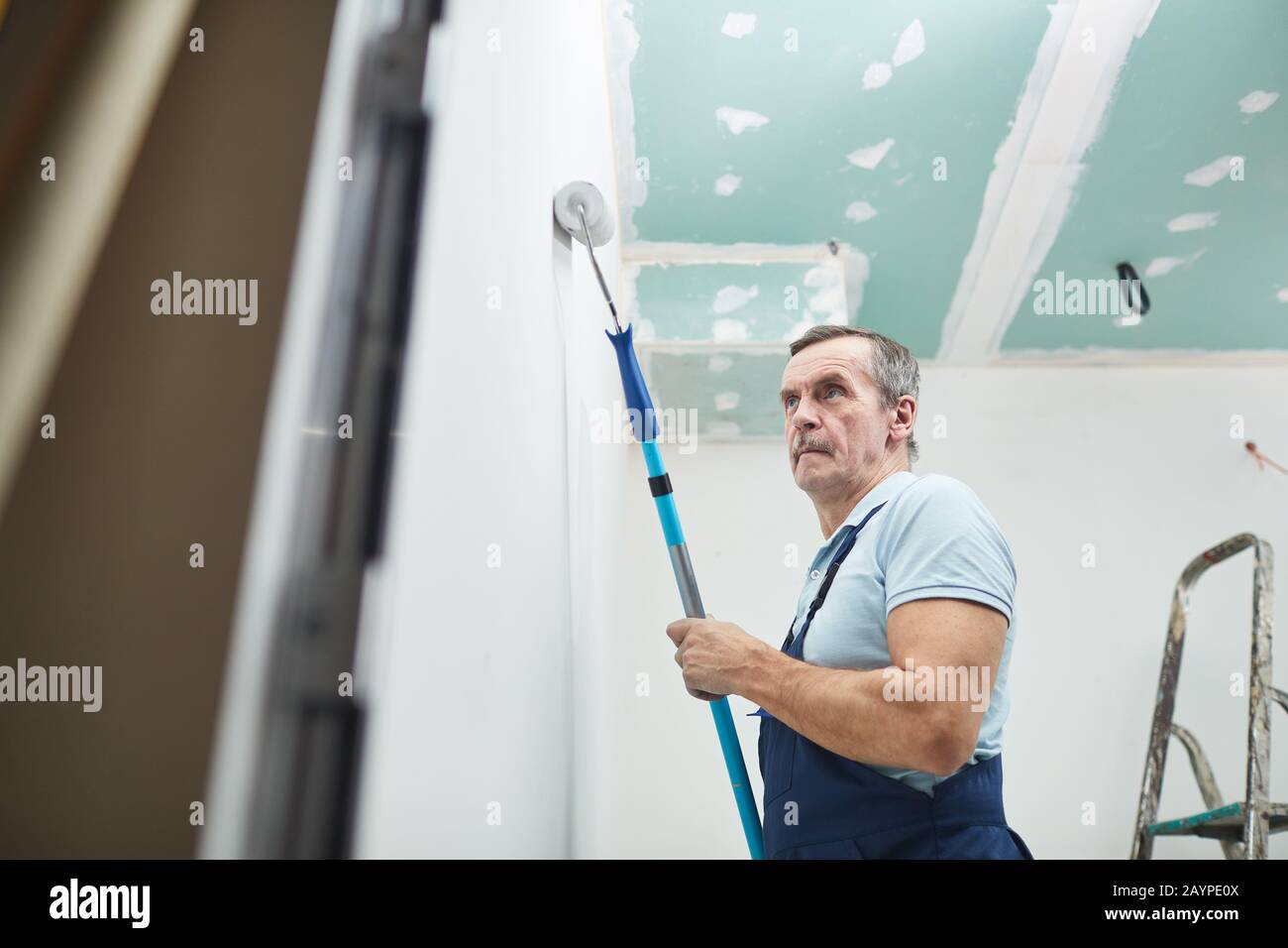 Low angle portrait of senior construction worker painting wall while renovating house, copy space Stock Photo