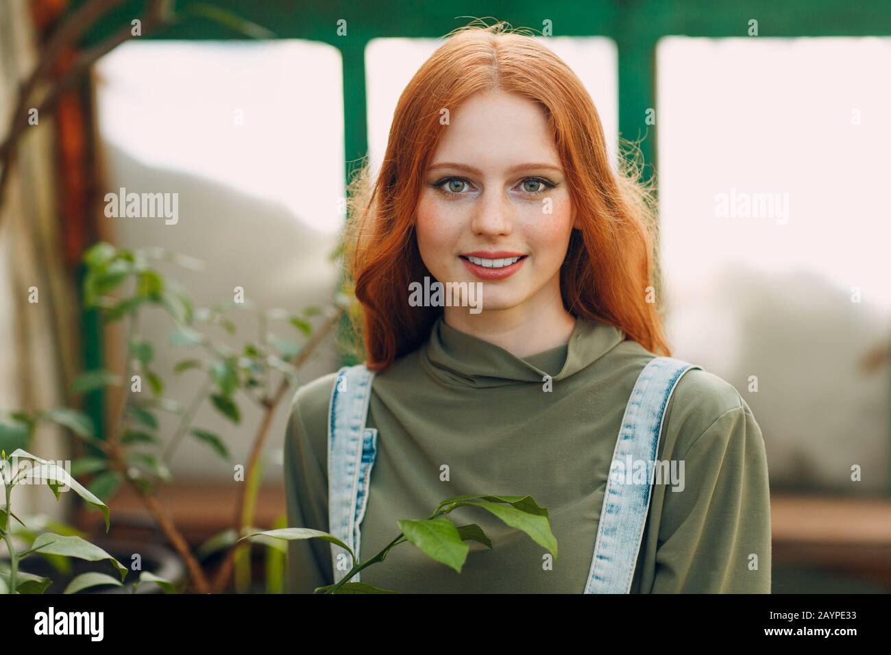 Young red hair woman farmer portrait looking camera and smile in greenhouse. Spring home gardening concept. Stock Photo