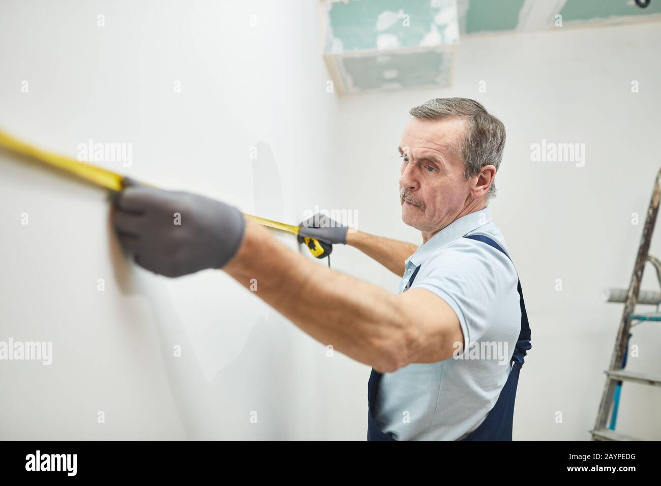 High angle portrait of senior construction worker measuring wall while renovating house, copy space Stock Photo