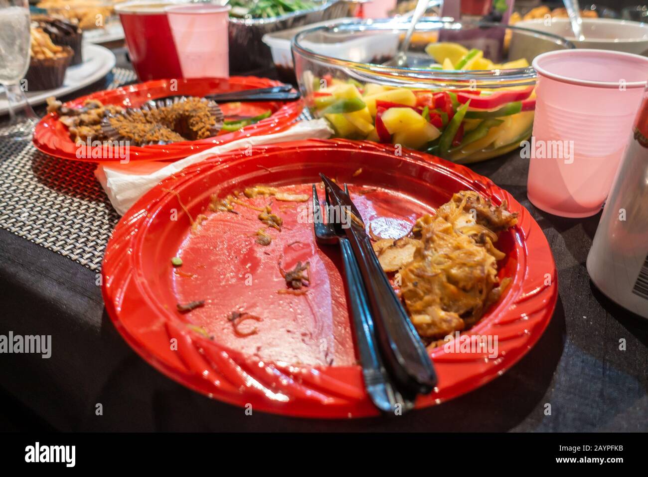 Red plastic disposable plate on a table after eating buffet food at a party Stock Photo