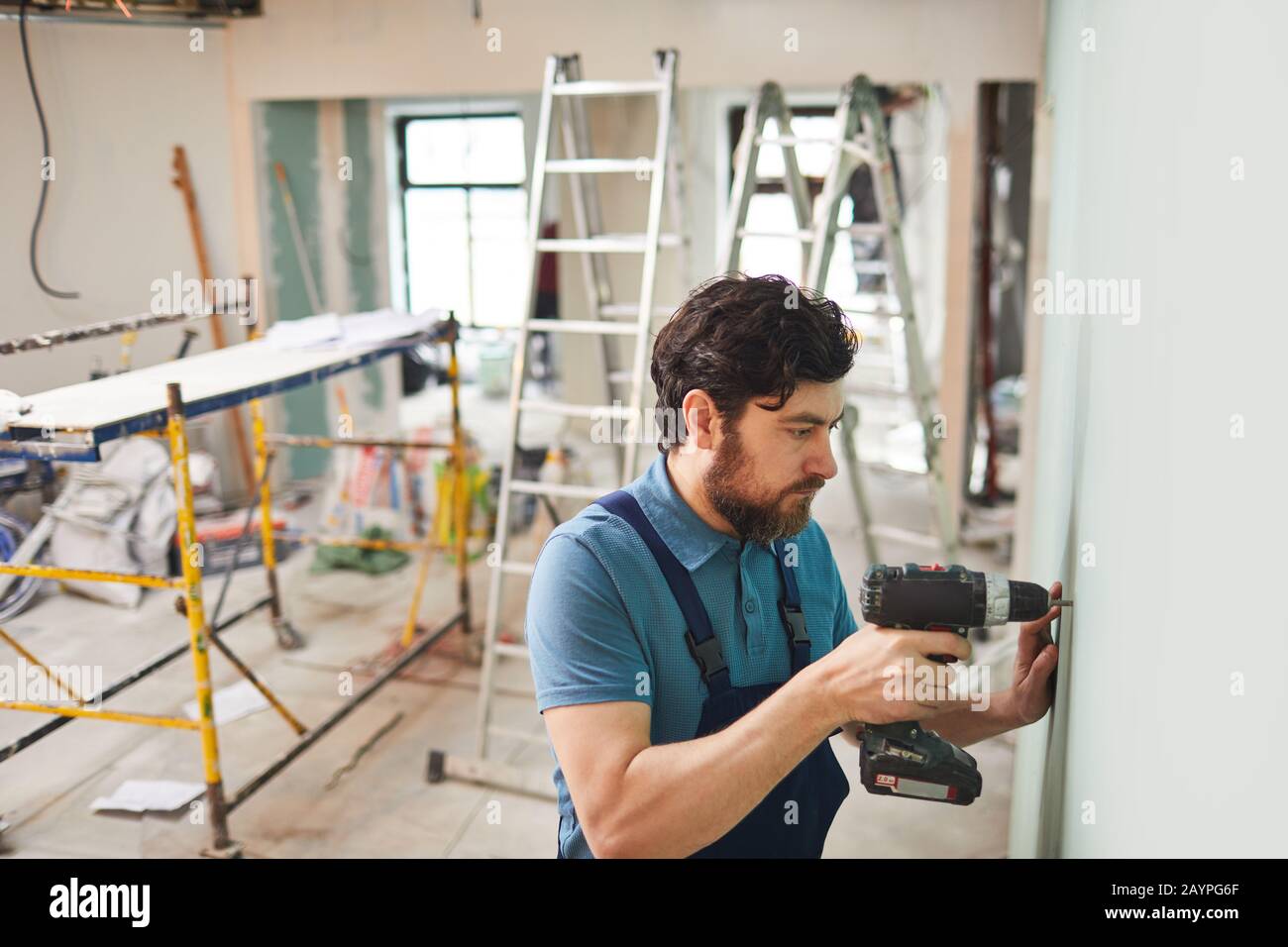 High angle portrait of bearded construction worker drilling wall while