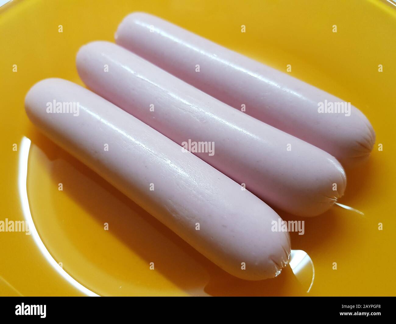 Three raw pink sausages lie in an orange plate Stock Photo Alamy