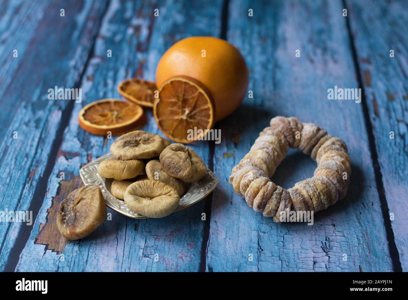 Sun-dried figs on a small plate. A dried fig wreath besprinkled with powdered sugar. A grapefruit and dried orange slices are in a blurry background. Stock Photo