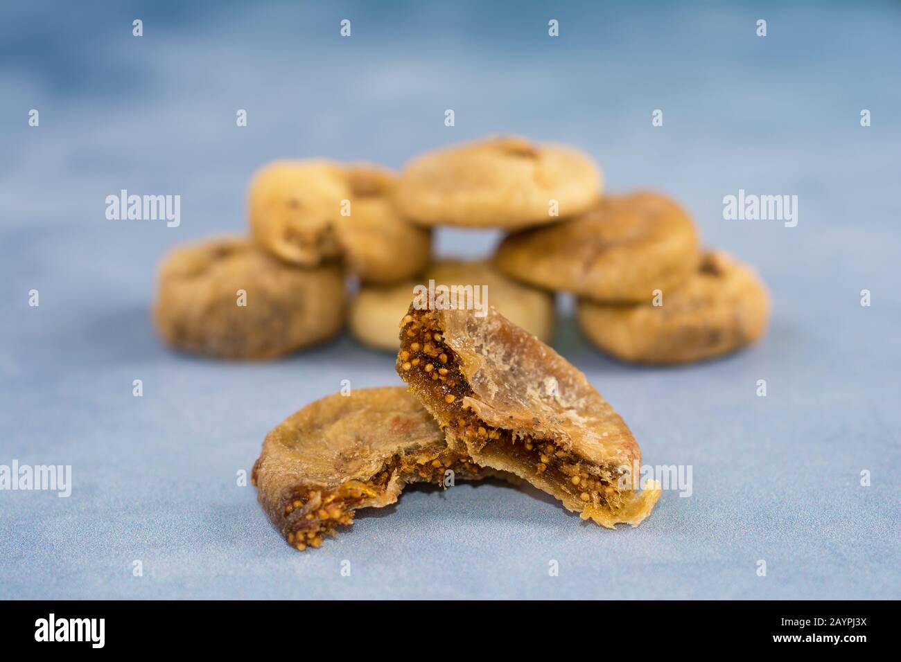 Dried figs. A mature common fig syconium torn apart, showing its numerous one-seeded fruits. A few dried figs stacked in a blurry background. Stock Photo