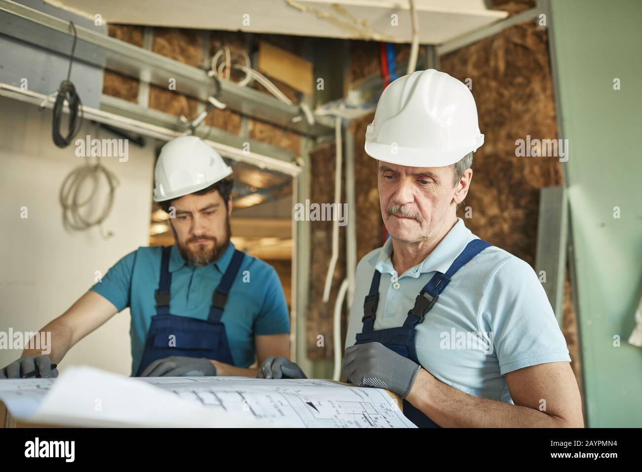 Portrait of senior construction worker wearing hardhat while looking at floor plans while renovating house, copy space Stock Photo