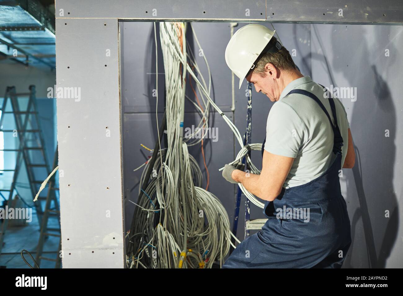 Back view portrait of senior electrician connecting cables in wires cabinet while renovating house, copy space Stock Photo