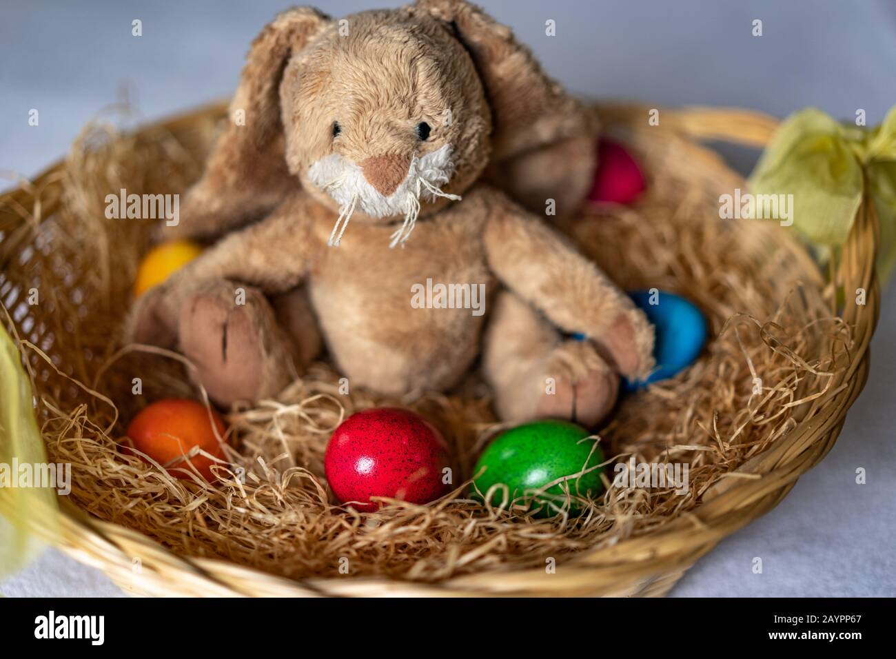 Stuffed easter bunny is sitting in straw basket with red, green, orange ...
