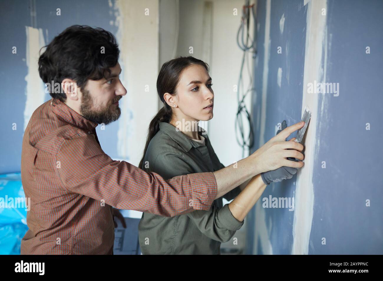 Waist up portrait of young couple smoothing dry wall while renovating house together, copy space Stock Photo