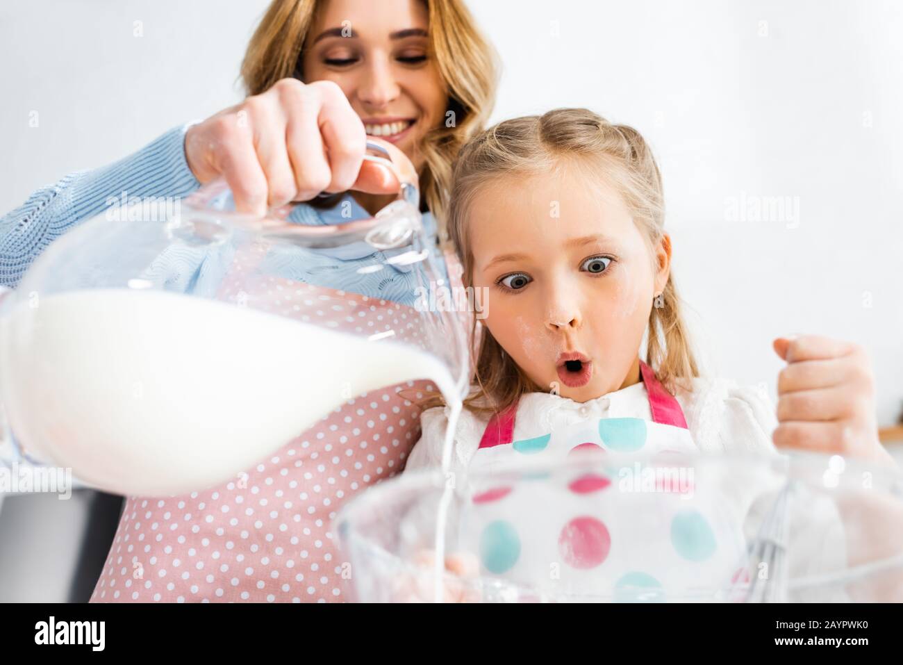 Low angle view of shocked daughter looking at mother pouring milk from jug in bowl Stock Photo