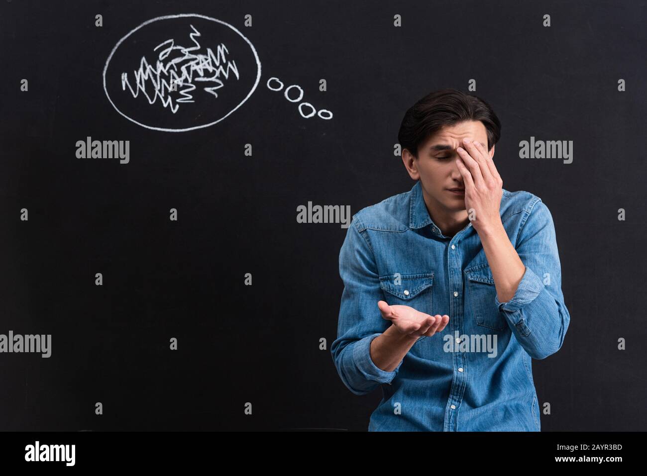 confused young man with thought bubble drawing on blackboard Stock Photo