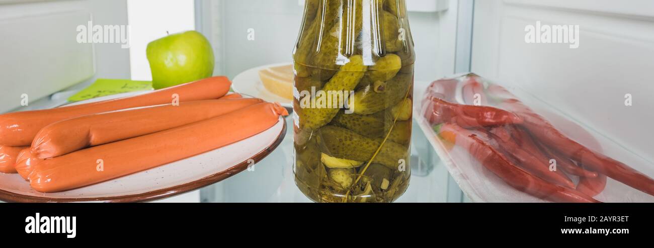Panoramic shot of sausages, pickles and chili peppers in fridge with open door isolated on white,stock image Stock Photo