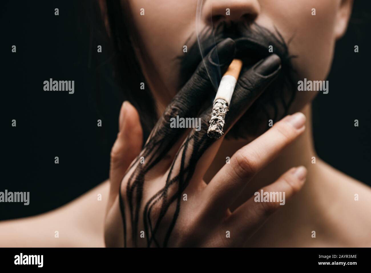 black lips cigarette Selective focus of woman with black painted hand and lips smoking cigarette  isolated on black Stock Photo