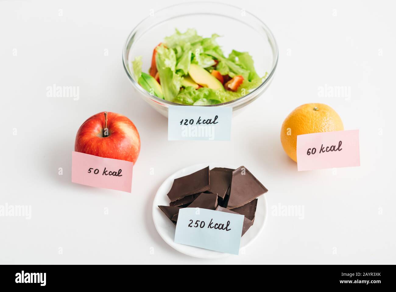 Fresh fruits, chocolate and salad with calories on cards on white background, calorie counting diet Stock Photo
