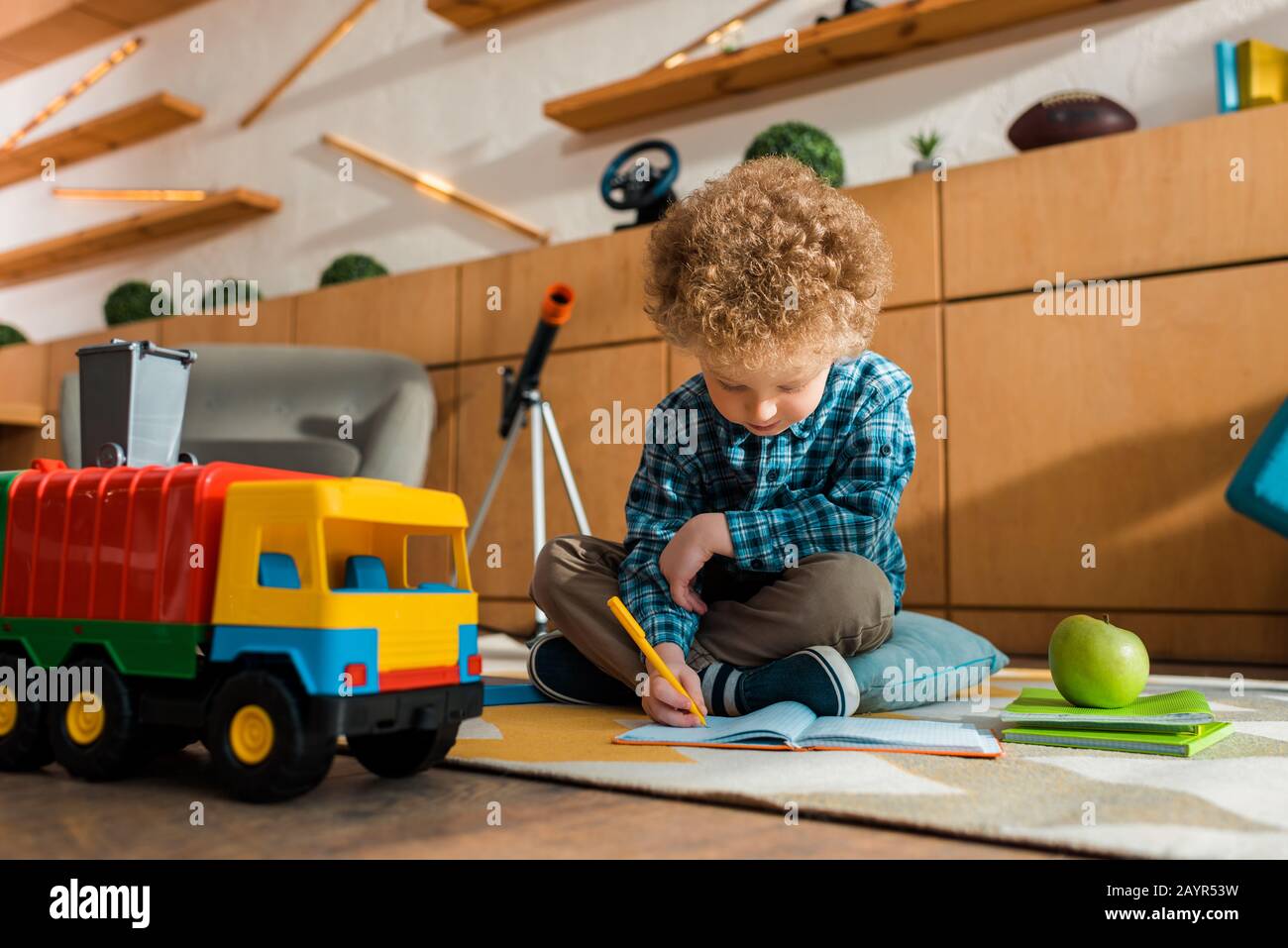 Smart Kid Writing In Notebook While Sitting On Floor Near Apple Toy Car And Books Stock Photo Alamy
