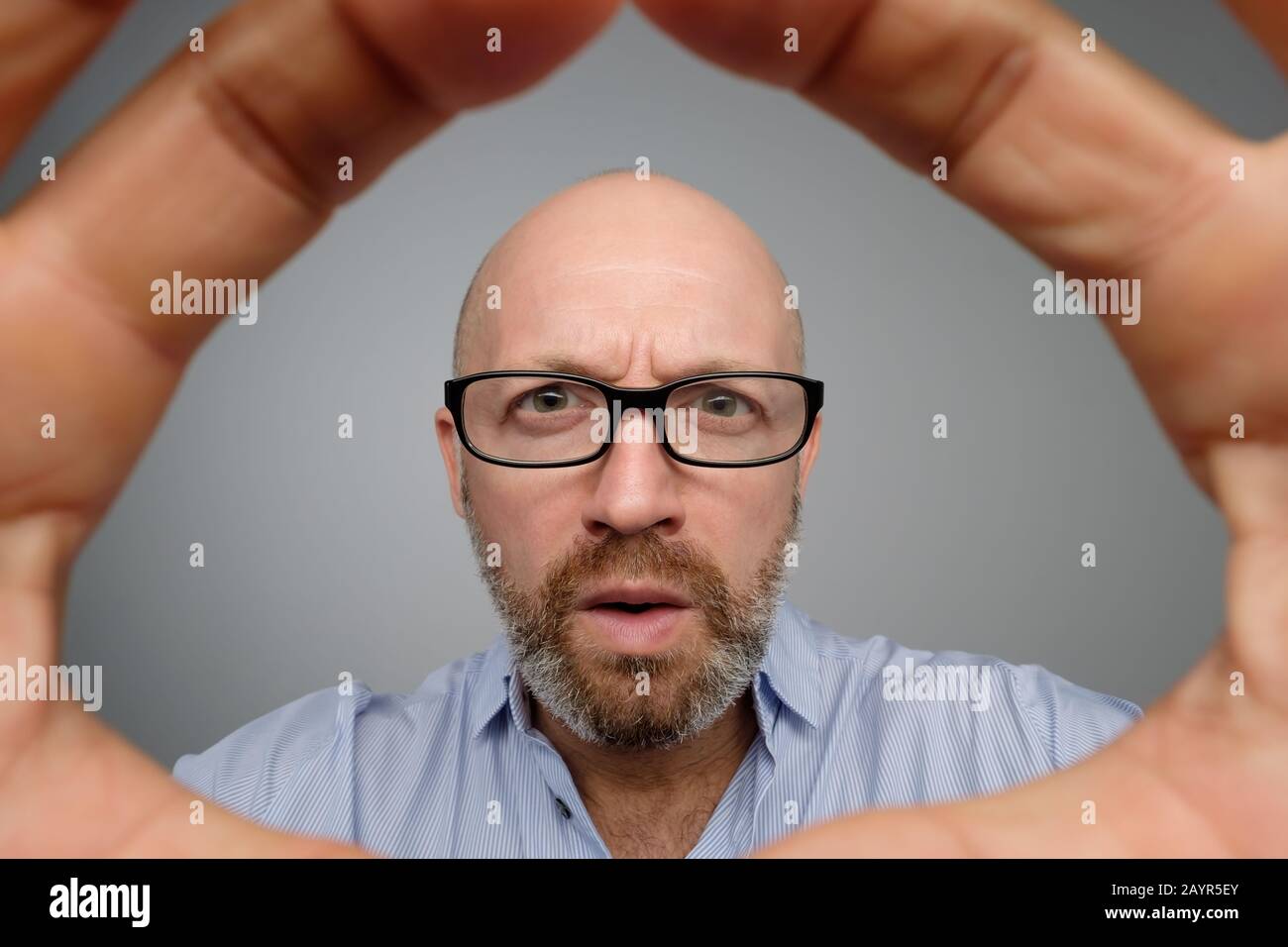 Bald mature guy in gray casual shirt discovering hidden camera. Hidden camera concept Stock