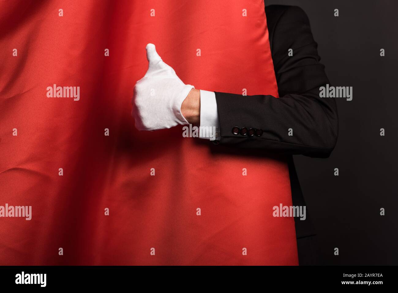 cropped view of magician in glove showing thumb up in circus with red curtains Stock Photo