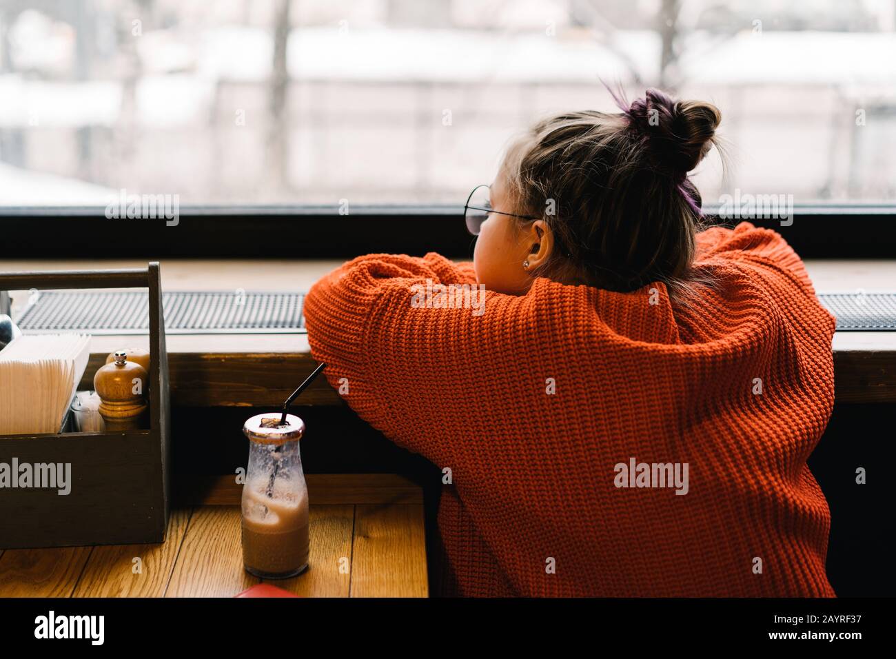 Girl teenager sitting in a cafe at a table waiting and looking out the window Stock Photo