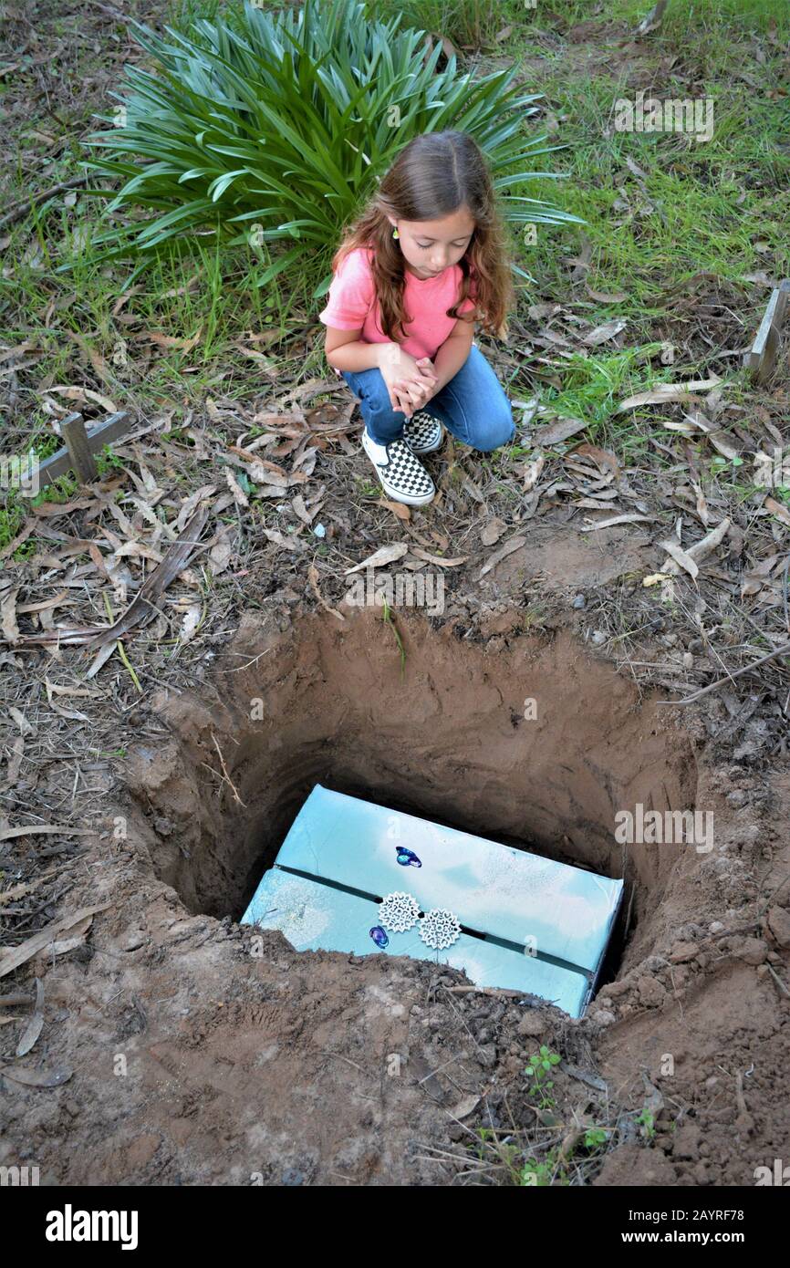 A sad 7 year old and her mom burying her real cat which died the night before of age and such in a grave in the back yard of her grandmothers home Stock Photo