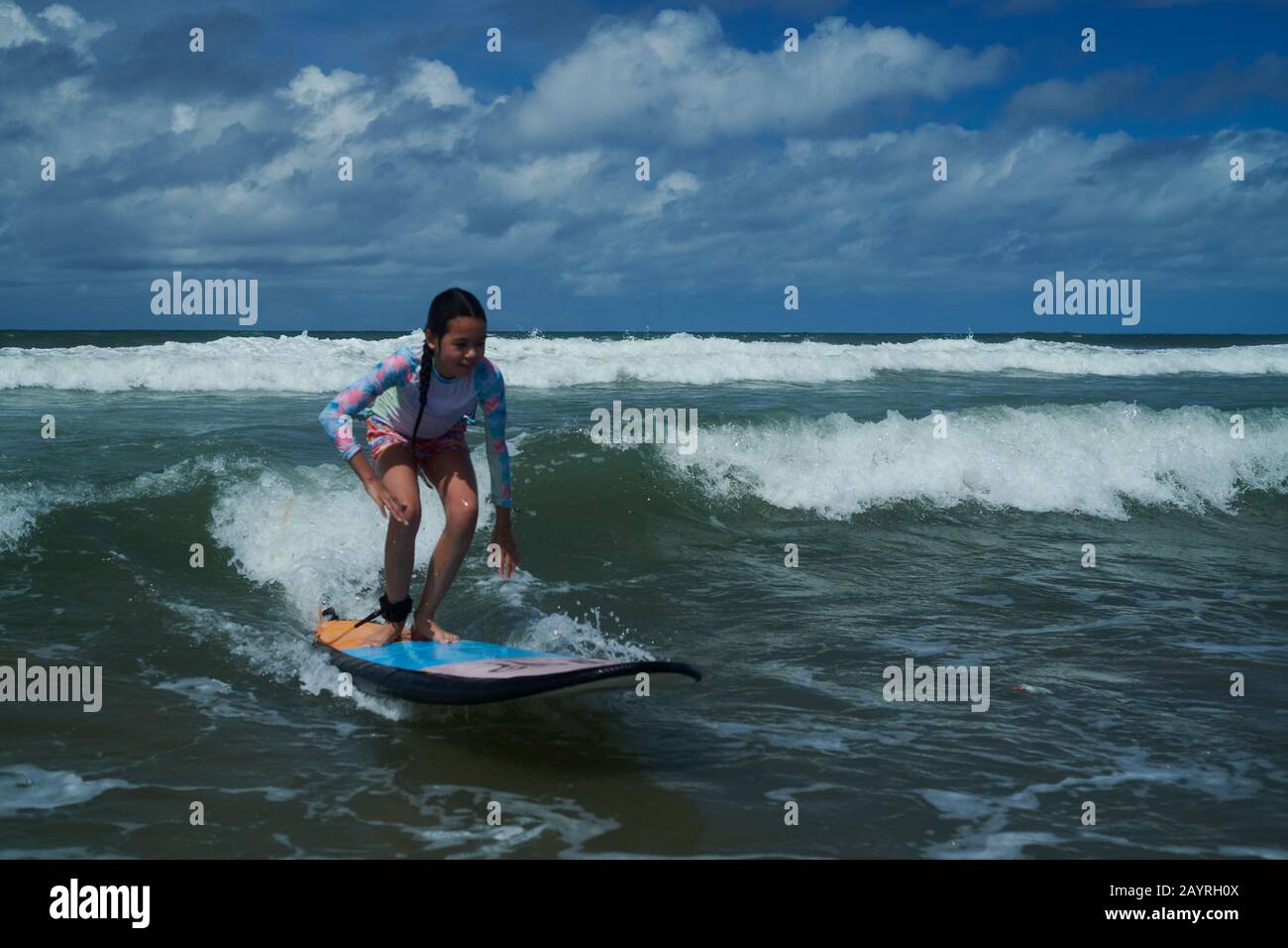 Young teen girl standing on a surf board catching her first wave during
