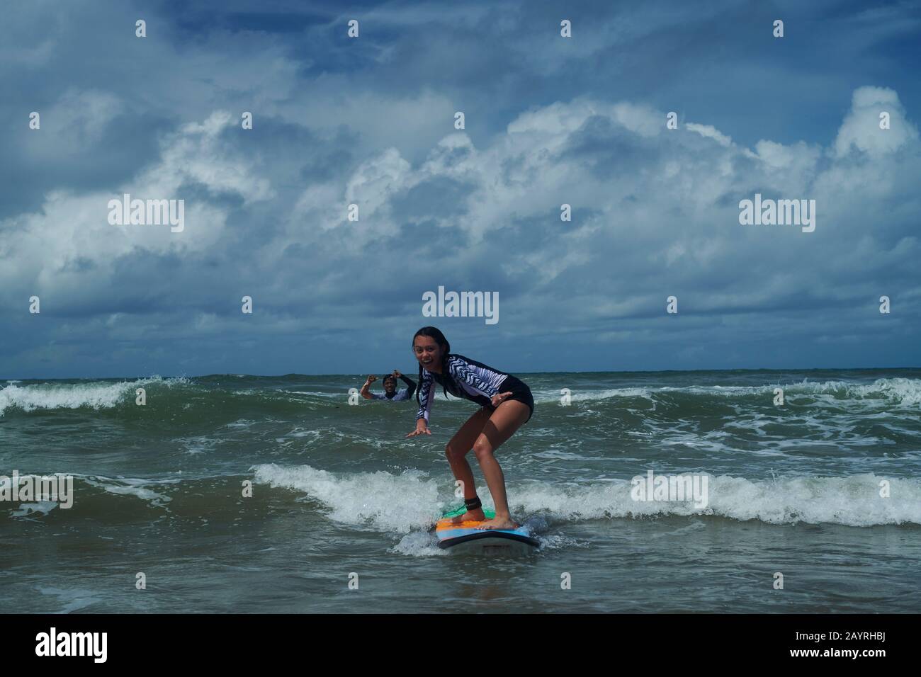 Young teen girl standing on a surf board catching her first wave during