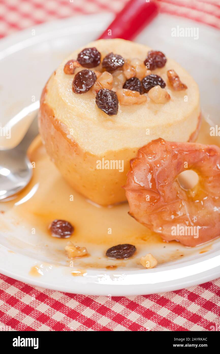 Honey baked apple with the core removed and filled with raisens and walnuts, and drizzled with honey, resting on a white ceramic plate Stock Photo