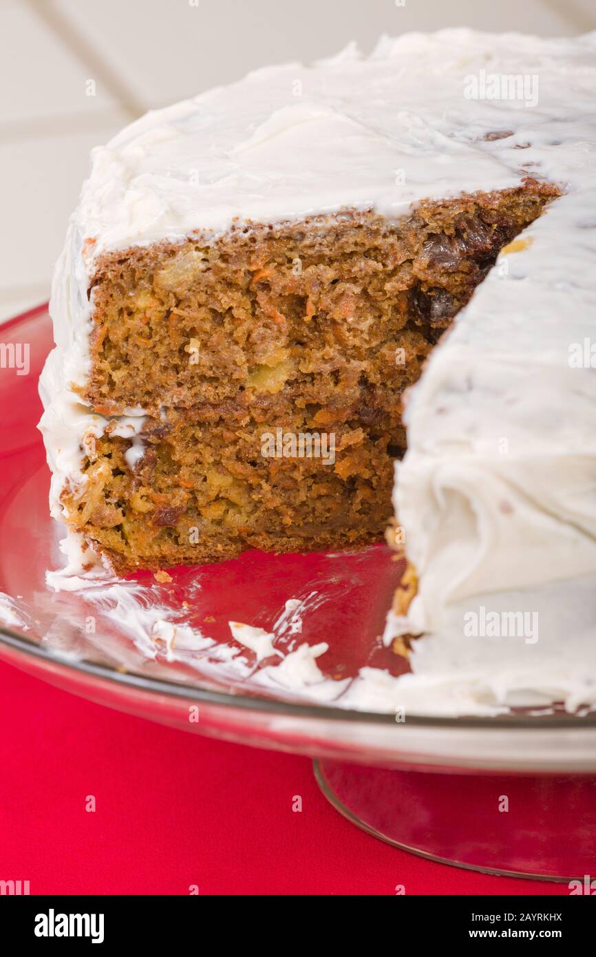 Whole carrot cake with a slice removed, resting on a glass cake stand Stock Photo