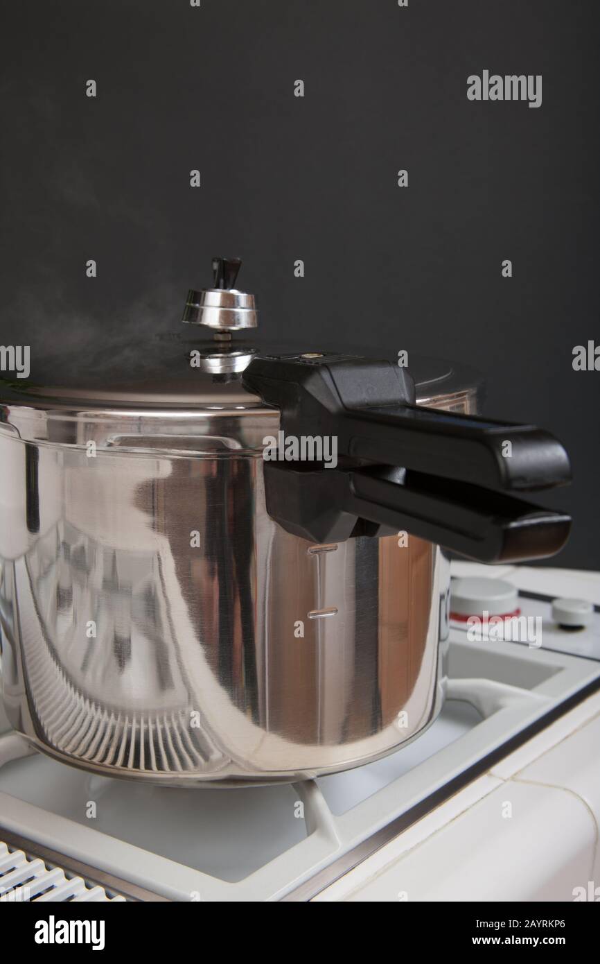 Pressure cooker on a stove with steam escaping as it cooks Stock Photo