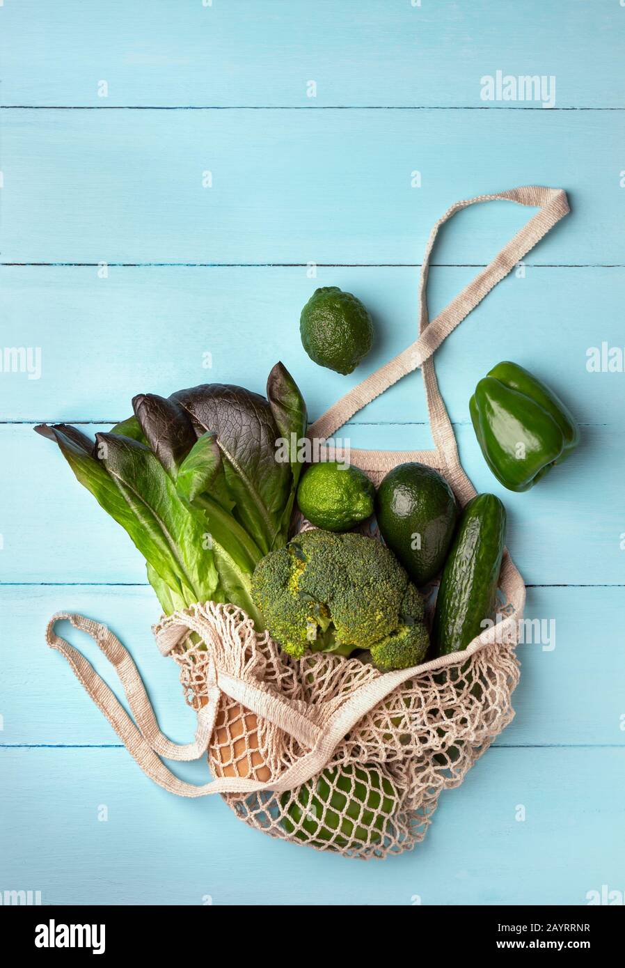 Green vegetables and fruits in a reusable string bag on a light blue background. Ecological concept, top view Stock Photo