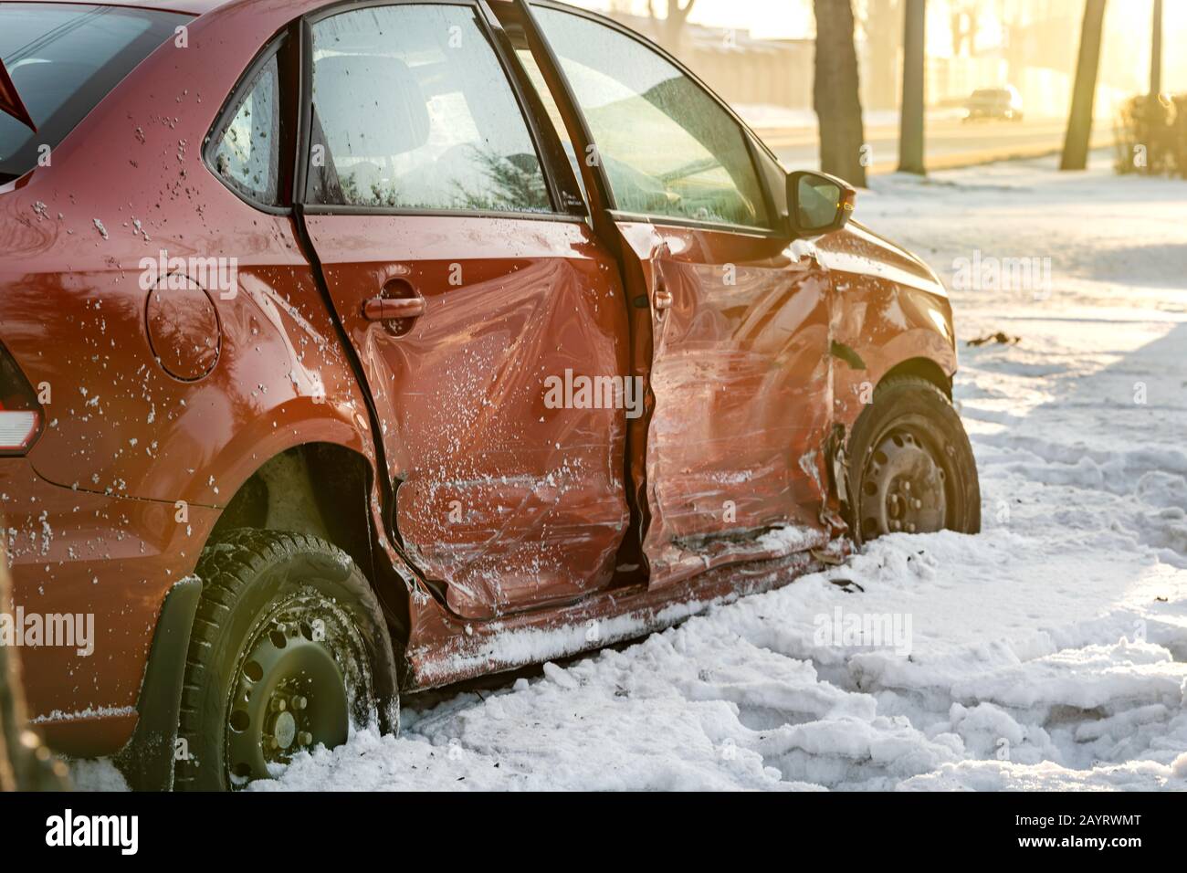 the broken and dented side of a red passenger car. winter accident on a slippery road, the car flew to the side of the road. Close-up, snow Stock Photo