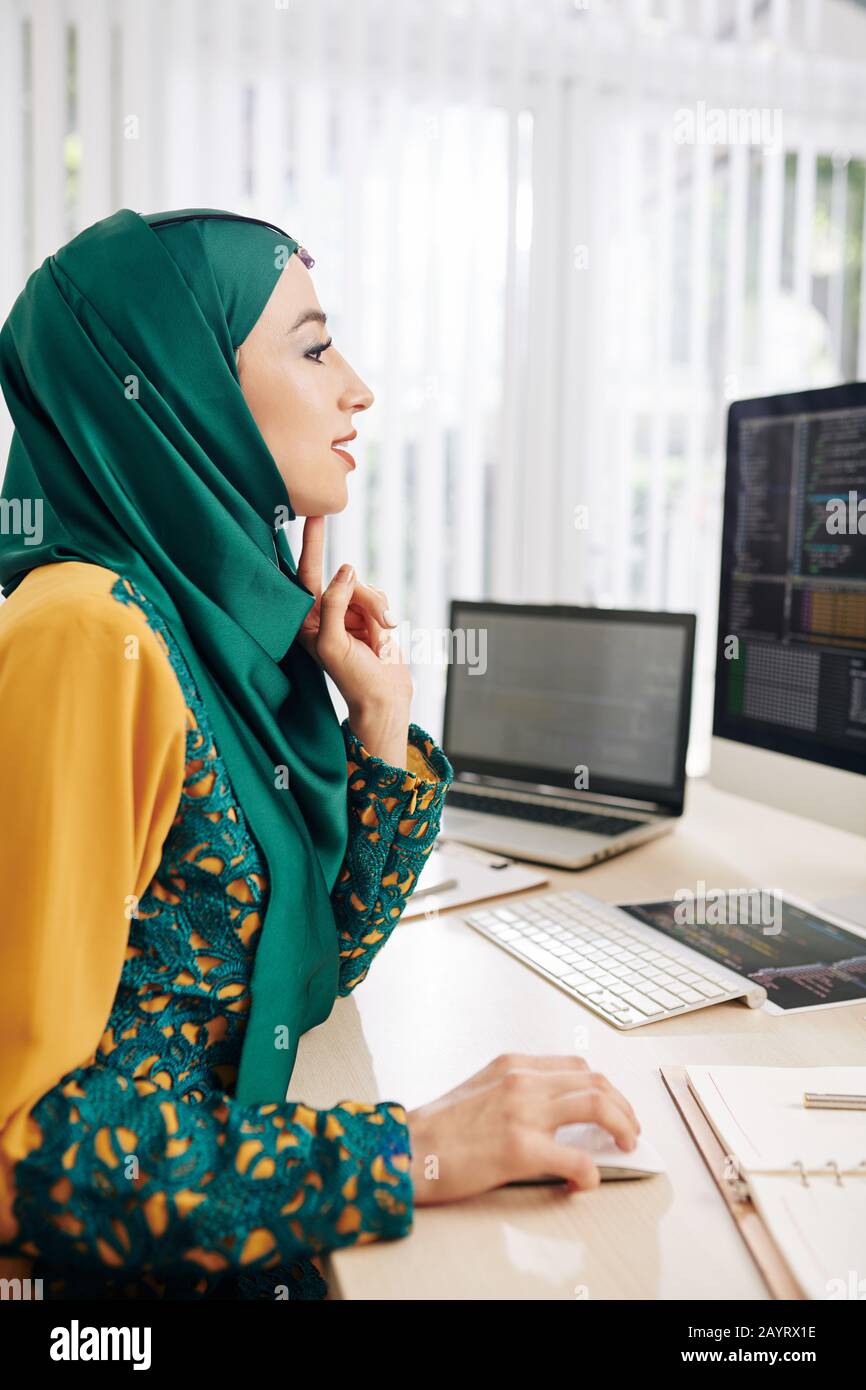 Excited female programmer sitting at office desk and writing code for mobile application Stock Photo