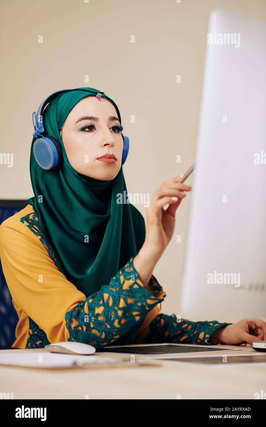 Serious female software developer in hedphones searching for mistakes in programming code on computer screen Stock Photo