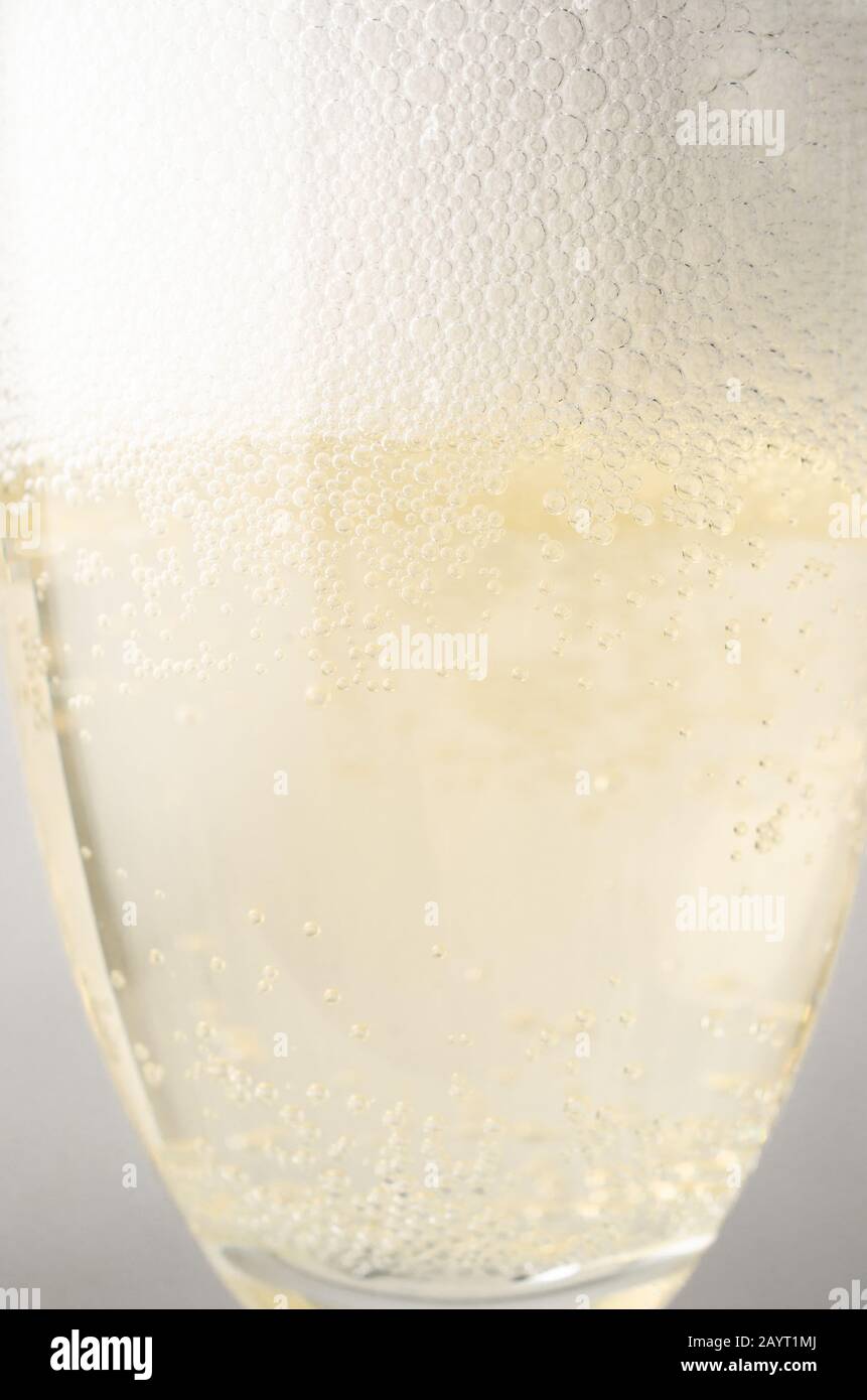 Close up (macro) eye level shot of a fluted glass freshly filled with champagne, topped with frothy white bubbles. Stock Photo