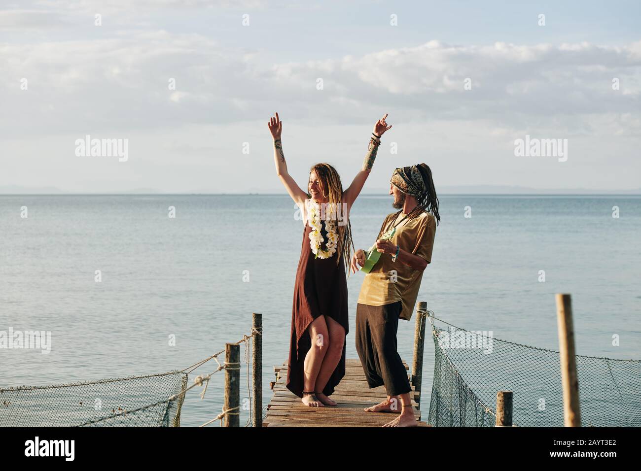 Cheerful man playing ukulele when his wife dancing on wooden pier Stock Photo